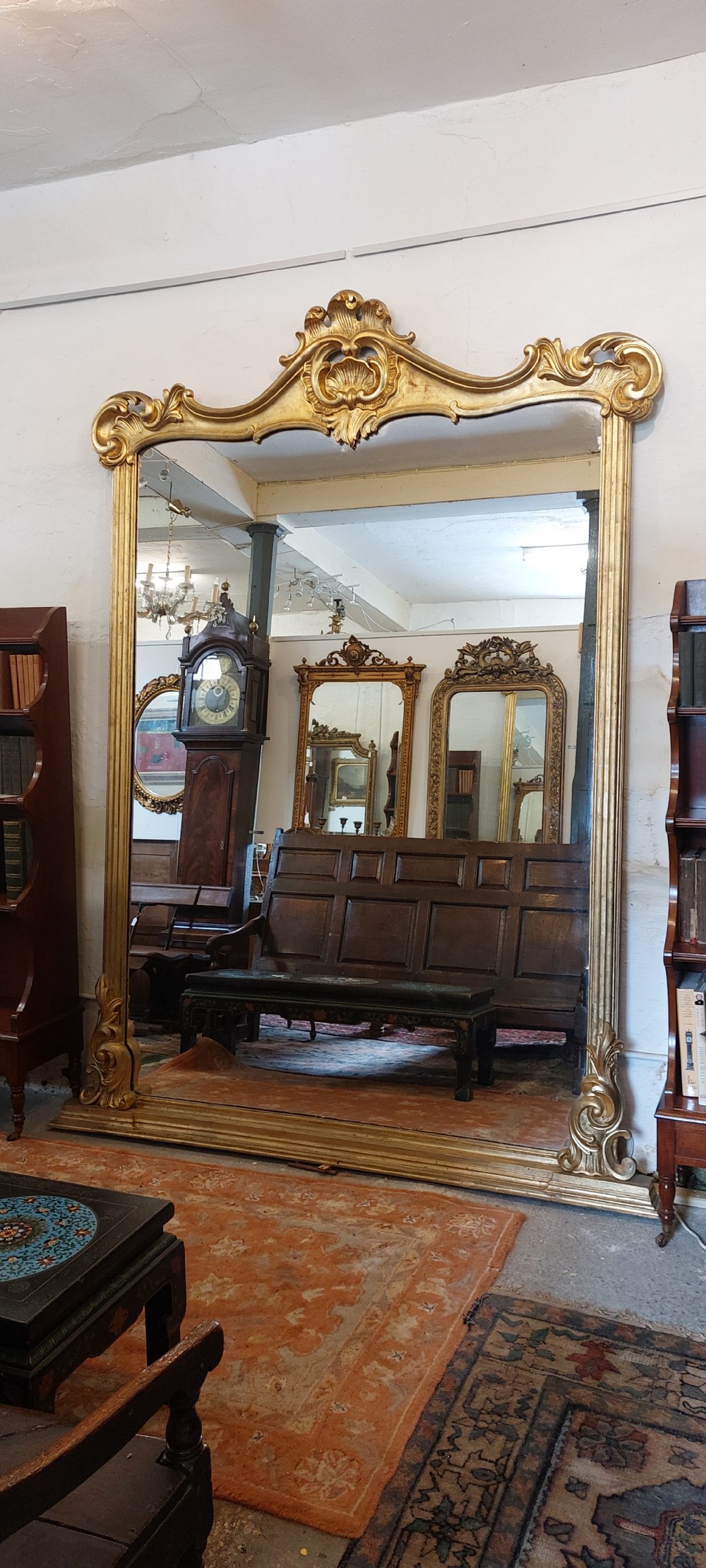 A large antique gold giltwood mirror with a decorative shell crest and carved scrollwork corner details.