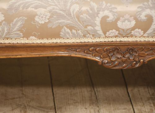 fig 3. A Louis XV style carved walnut settee upholstered in beige damask fabric, featuring cabriole legs, padded armrests, and a carved cresting rail.