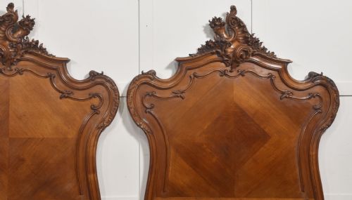 fig 2. A matching pair of carved walnut single bed frames with high crest headboards, serpentine footboards, and book-matched timber panels.