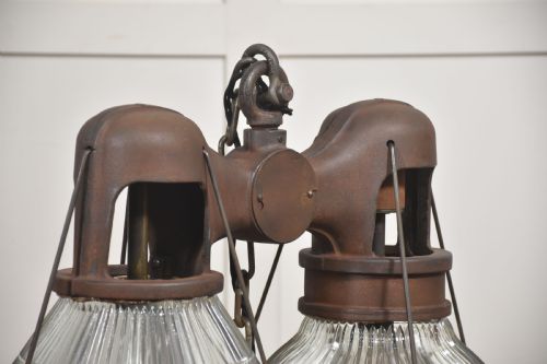 fig 2. A pair of double-dome industrial pendant lights featuring clear ribbed Holophane glass shades set in dark brown metal frames with chain supports.