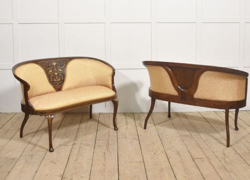 fig 2. A matching pair of Edwardian mahogany settees featuring curved backs, floral marquetry central splats, and pale mustard yellow upholstered seats.
