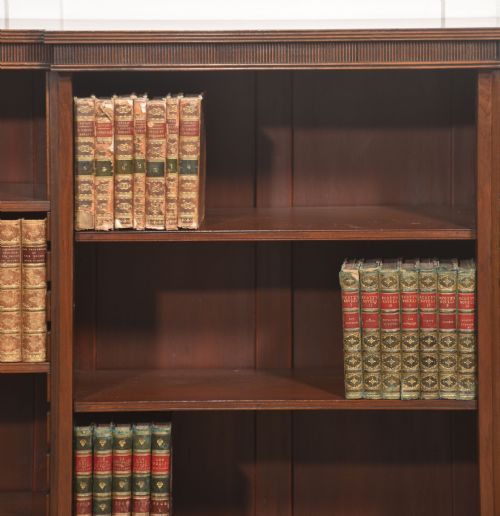 fig 1. A low mahogany breakfront open bookcase featuring a reeded frieze top, adjustable shelf sections, and bracket feet.
