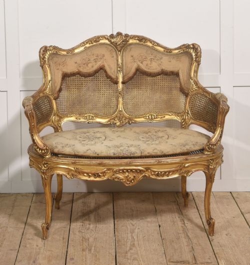 fig 1. A French Louis XV style giltwood canape featuring a carved frame, caned back and sides, cabriole legs, and an upholstered seat cushion.
