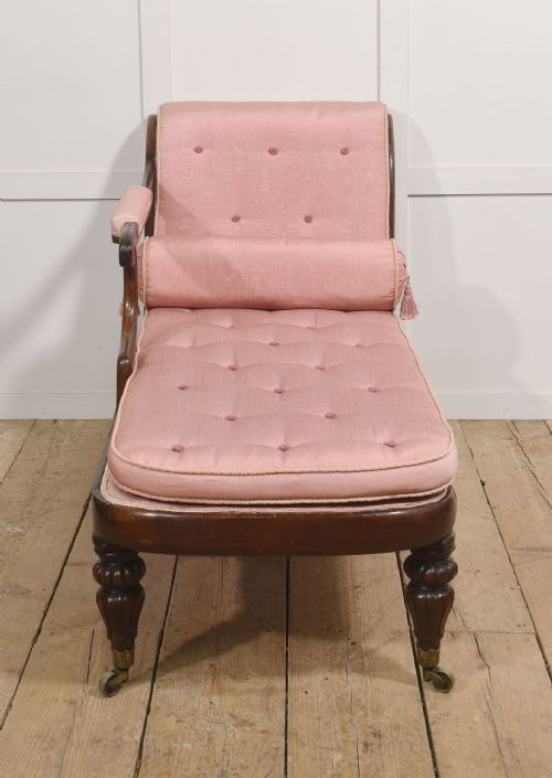 fig 1. A William IV rosewood chaise longue upholstered in pink fabric with a matching bolster cushion and turned legs on brass castors.