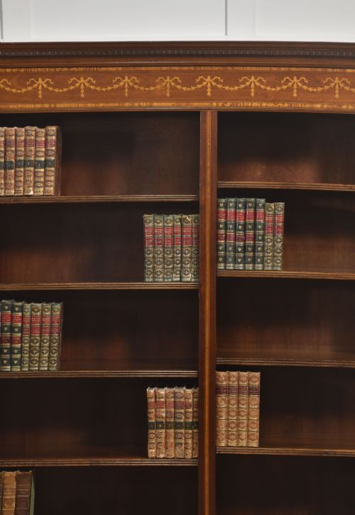 fig 2. A tall, double-bay mahogany open bookcase featuring delicate satinwood festoon inlays along the top frieze and multiple fixed shelves containing books.