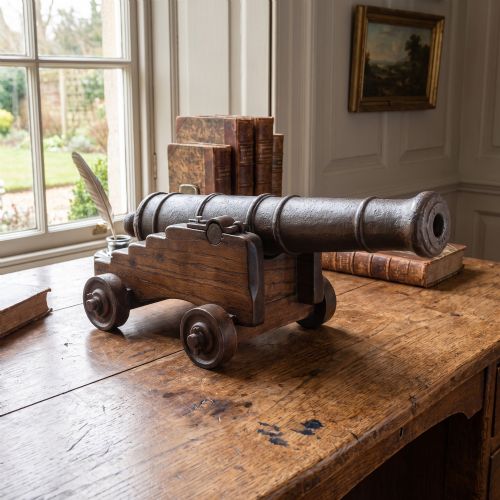 fig 1. A miniature cast-iron signal cannon barrel mounted on a dark stepped oak wooden carriage with four wooden wheels.