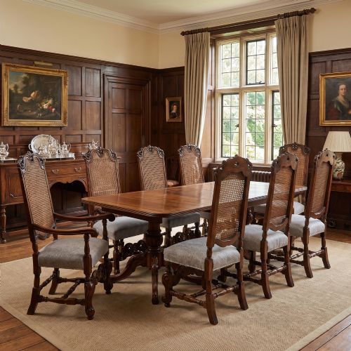 fig 1. A set of eight walnut dining chairs featuring tall carved frames, woven cane back panels, grey upholstered seats, and scrollwork stretchers.