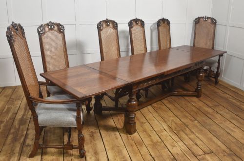 fig 2. A set of eight walnut dining chairs featuring tall carved frames, woven cane back panels, grey upholstered seats, and scrollwork stretchers.