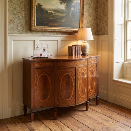 fig 1. A Sheraton Revival bow-front wooden sideboard featuring oval inlaid veneer door panels, top drawers, and square tapered legs.