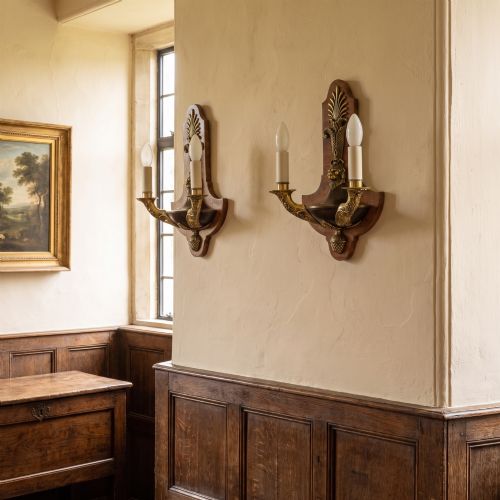 fig 1. A pair of Empire style wall lights featuring shaped burr walnut backplates decorated with brass lion masks, anthemion crests, and twin scrolling candle arms.