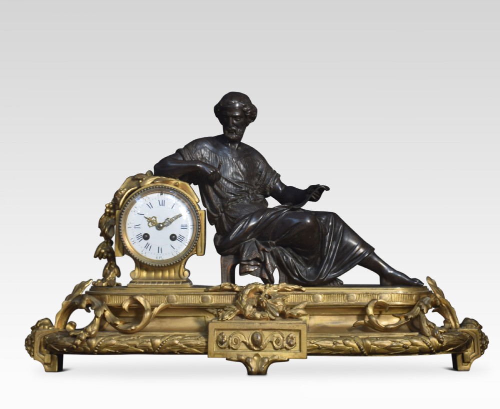 A late 19th-century French gilt metal mantel clock featuring a dark bronze classical figure seated beside an enamel dial on an ornate gilded scroll base.