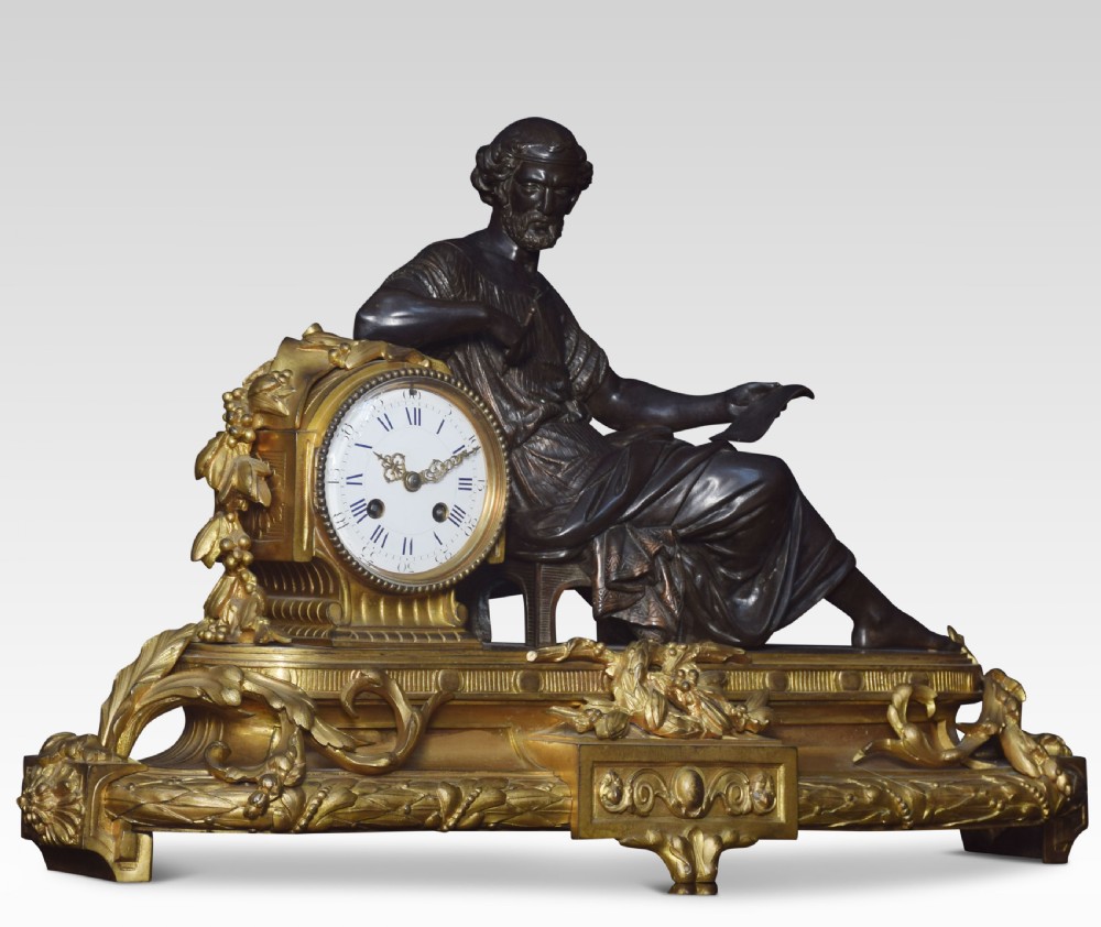 A late 19th-century French gilt metal mantel clock featuring a dark bronze classical figure seated beside an enamel dial on an ornate gilded scroll base. View II