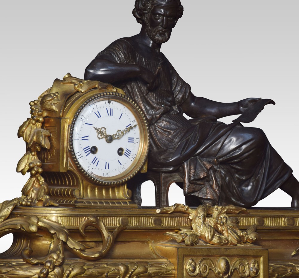 A late 19th-century French gilt metal mantel clock featuring a dark bronze classical figure seated beside an enamel dial on an ornate gilded scroll base. View III
