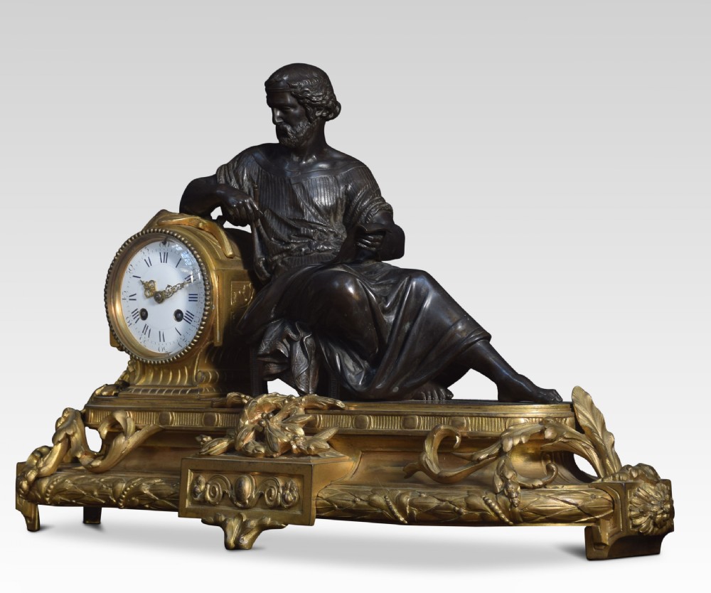 A late 19th-century French gilt metal mantel clock featuring a dark bronze classical figure seated beside an enamel dial on an ornate gilded scroll base. View V