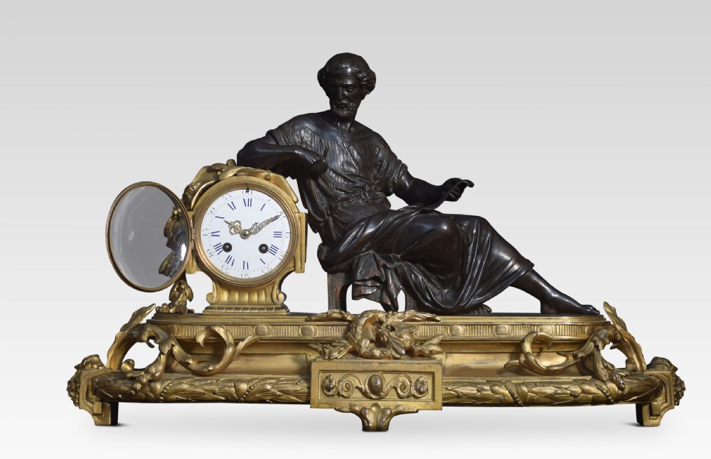 A late 19th-century French gilt metal mantel clock featuring a dark bronze classical figure seated beside an enamel dial on an ornate gilded scroll base. View VII