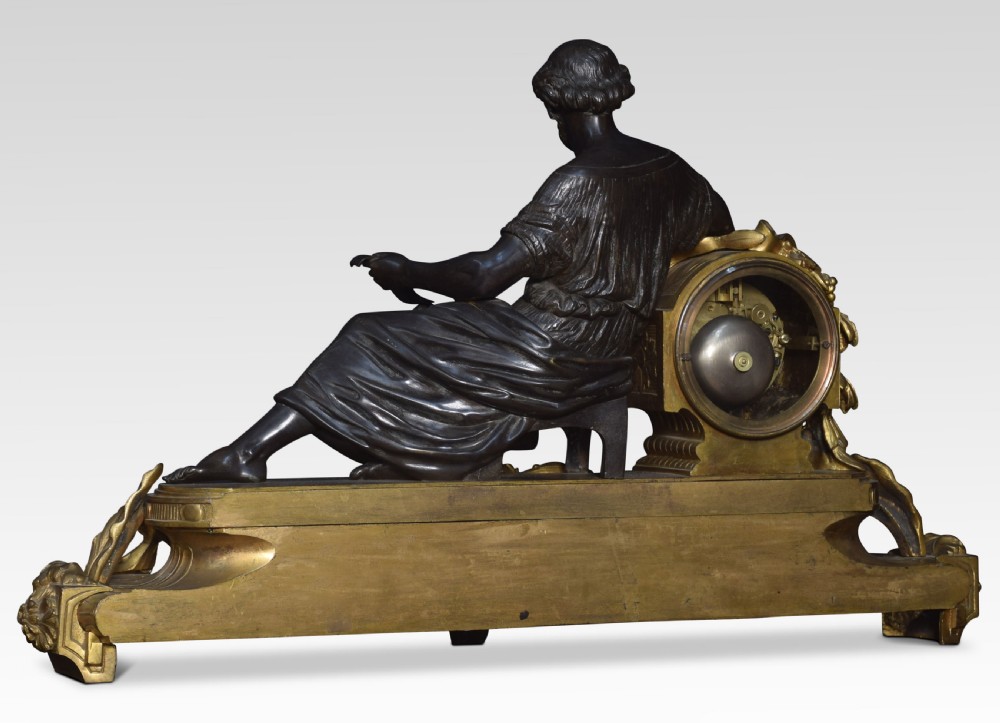 A late 19th-century French gilt metal mantel clock featuring a dark bronze classical figure seated beside an enamel dial on an ornate gilded scroll base. View VIII