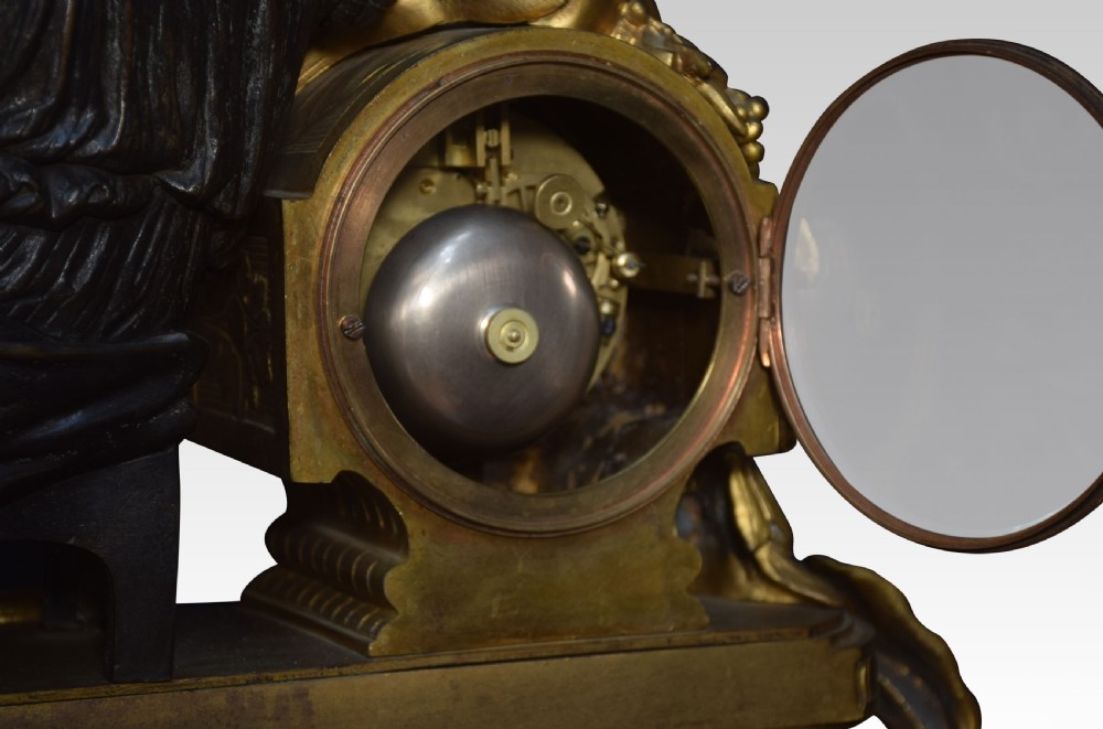 A late 19th-century French gilt metal mantel clock featuring a dark bronze classical figure seated beside an enamel dial on an ornate gilded scroll base. View IX
