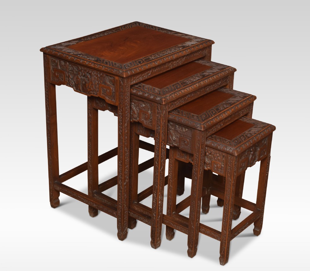 A set of four graduating Chinese hardwood nesting tables featuring relief-carved aprons and geometric borders.