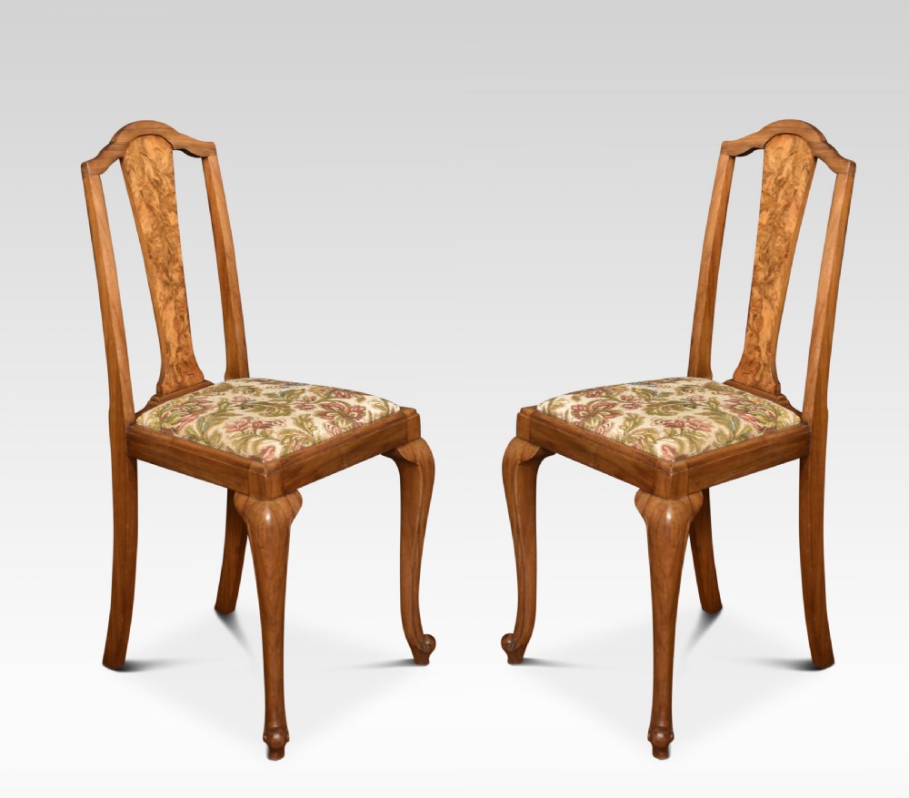 A pair of antique walnut side chairs featuring high backs with central burr walnut splats, floral upholstered seats, and curved cabriole legs.
