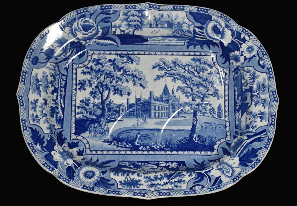 An oval 19th-century Staffordshire ceramic platter featuring a cobalt blue transfer-printed landscape scene with a stately home surrounded by intricate floral borders.
