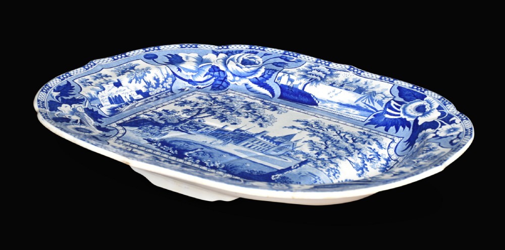 An oval 19th-century Staffordshire ceramic platter featuring a cobalt blue transfer-printed landscape scene with a stately home surrounded by intricate floral borders. View V