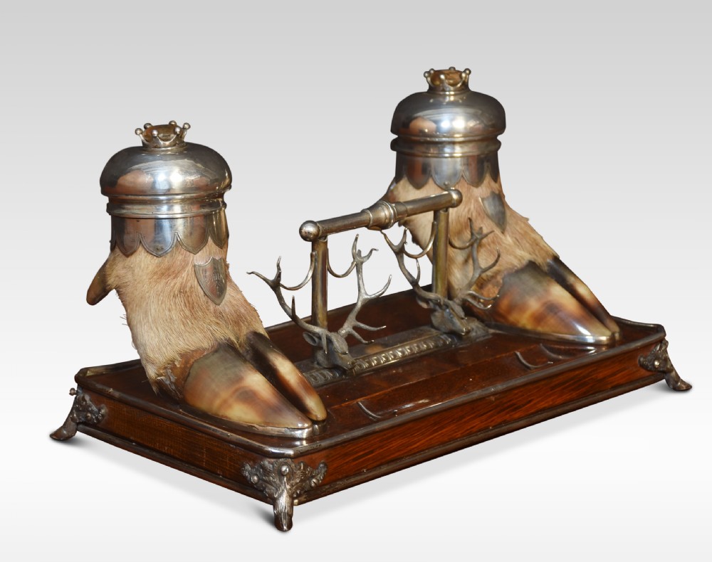 A 19th-century Scottish double inkwell set featuring two silver-capped deer hooves and stag head pen rests mounted on a mahogany base.