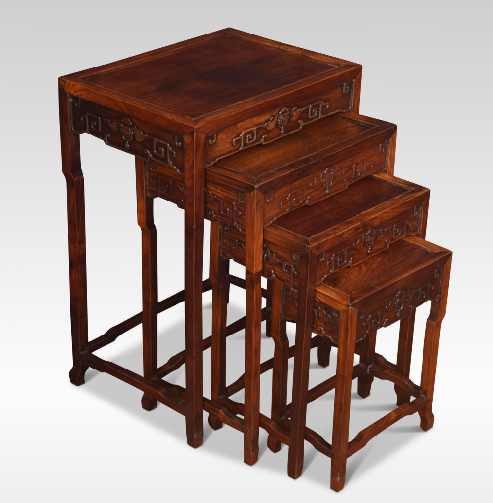 A set of four graduated dark rosewood nesting tables with carved openwork aprons and straight legs.