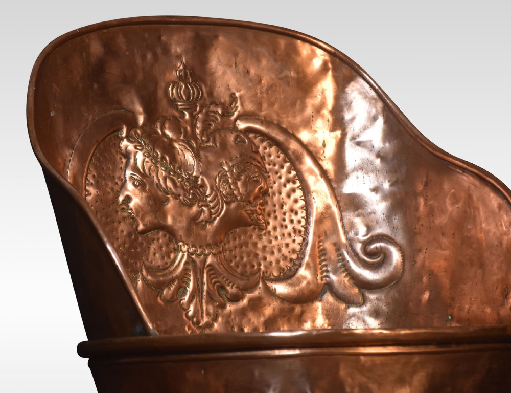 A tall, tapered 19th-century copper log bin featuring a hand-hammered body, raised repousse classical medallion crest, and a scooped upper rim. View II