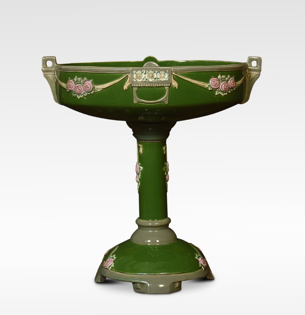 An Art Nouveau green glazed ceramic pedestal centrepiece bowl decorated with pink floral relief swags and low handles.