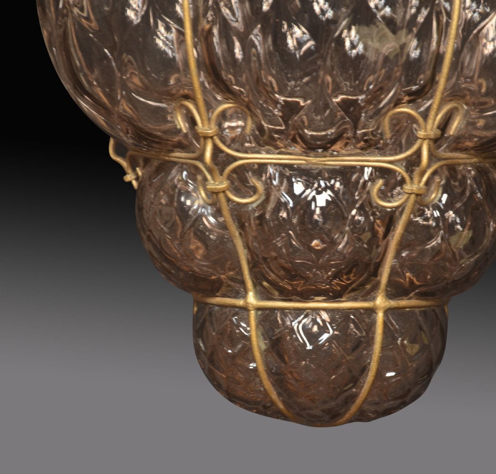 A hand-blown purple glass pendant light encased within a decorative brass wire cage structure. View III