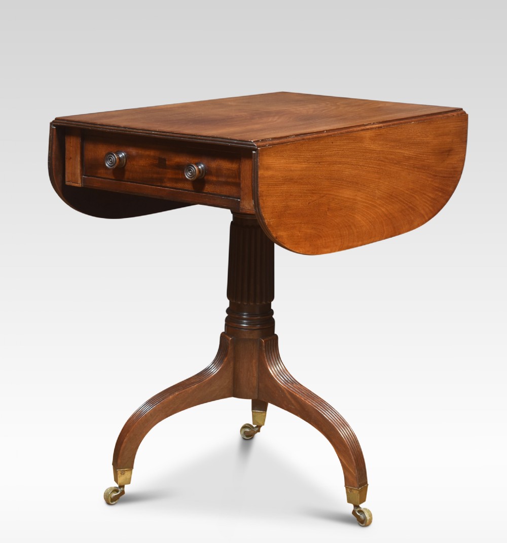 A Regency mahogany Pembroke end table featuring two drop leaves, a single frieze drawer, a reeded pedestal stem, and tripod legs with brass castors.