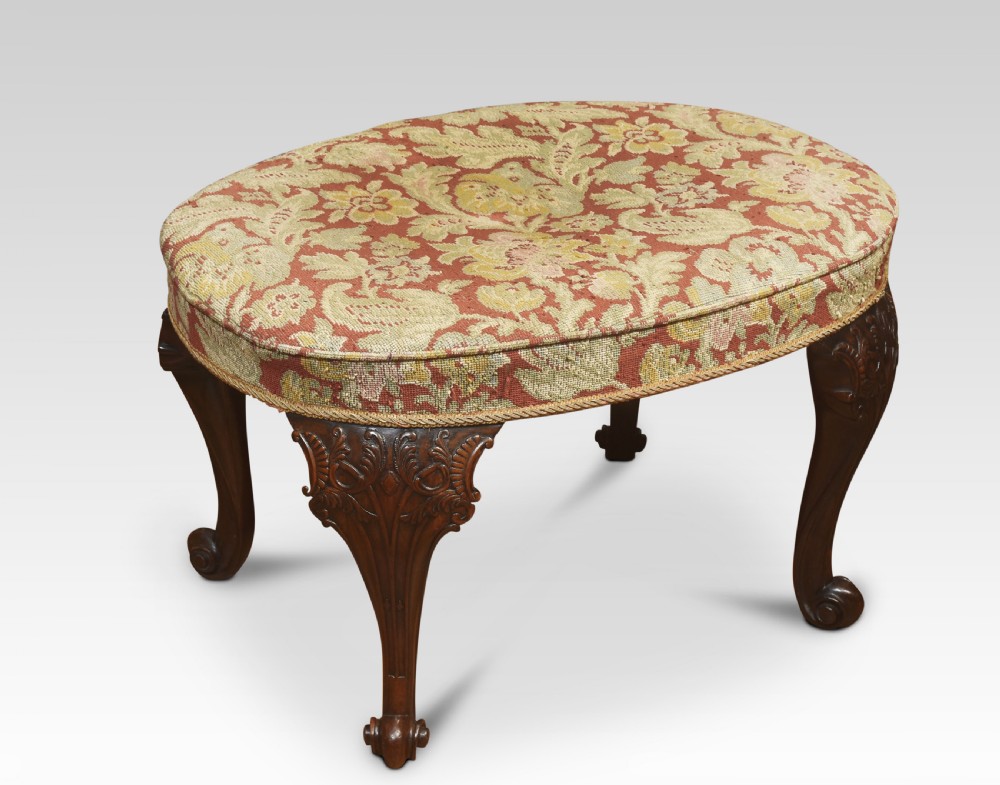 An oval George II style stool featuring patterned tapestry upholstery, carved mahogany cabriole legs, and scroll feet.