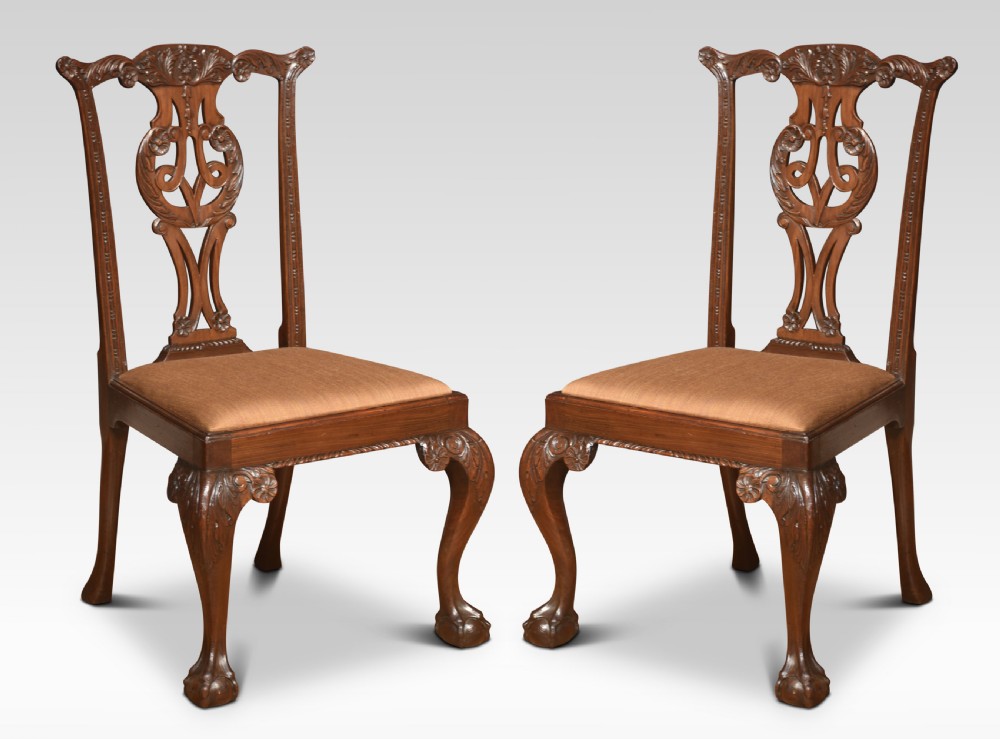 A pair of Chippendale Revival mahogany side chairs with carved pierced back splats, cabriole legs terminating in claw and ball feet, and light brown upholstered seats.