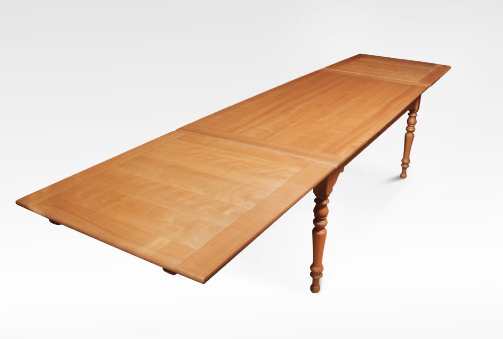 A large fruitwood farmhouse dining table featuring a framed plank top with breadboard ends and turned legs.