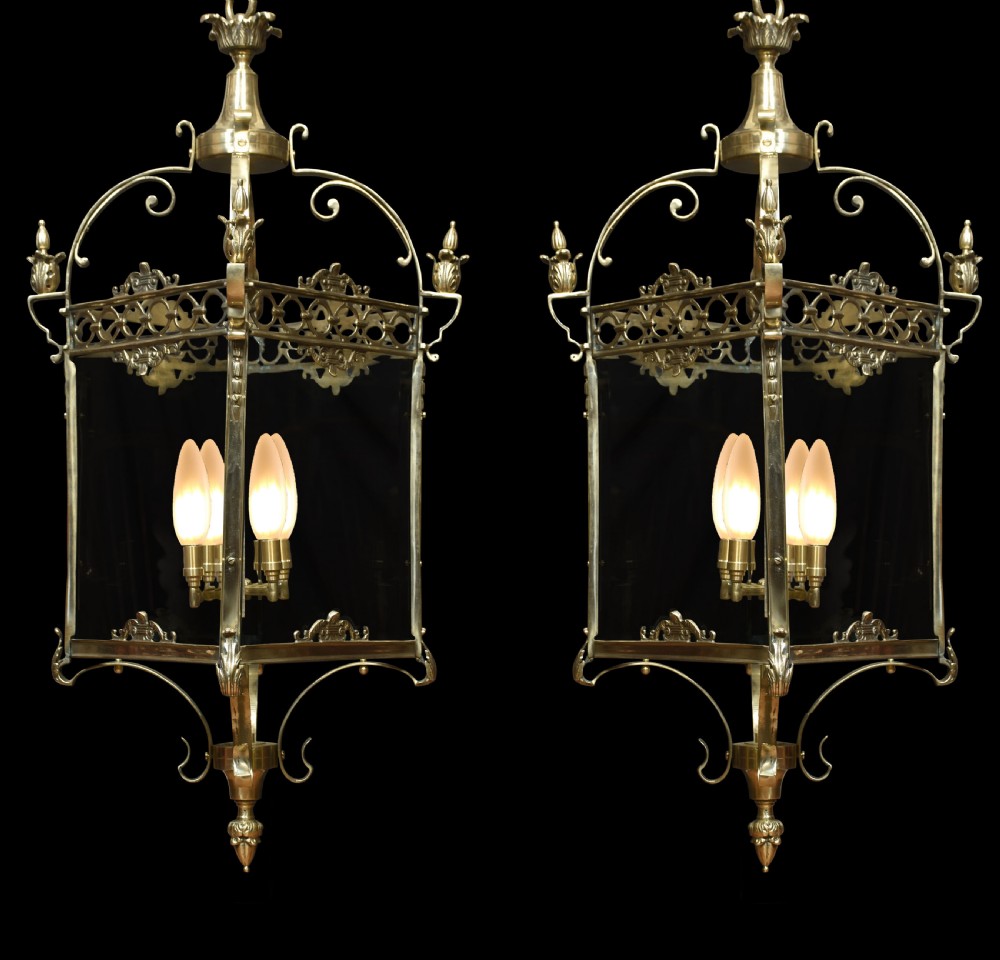 A pair of large brass hall lanterns with decorative scrollwork, glass side panels, finials, and internal four-bulb fittings.