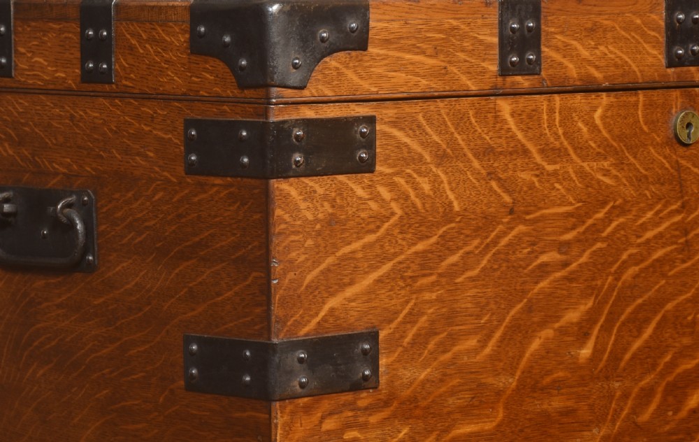 A 19th-century oak silver chest reinforced with black iron corner brackets and strapwork, shown with its lid open to display a blue padded fabric interior lining. View II