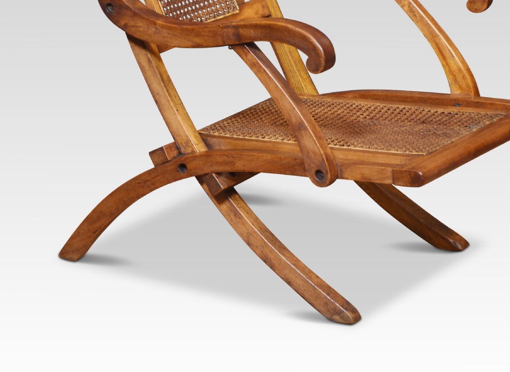 An antique walnut folding steamer chair featuring a reclined timber frame, curved armrests, and woven cane panels on the backrest and seat. View V