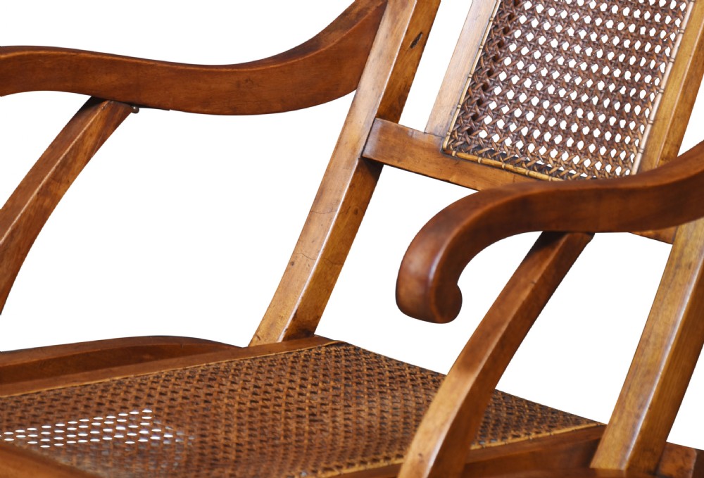 An antique walnut folding steamer chair featuring a reclined timber frame, curved armrests, and woven cane panels on the backrest and seat. View VI