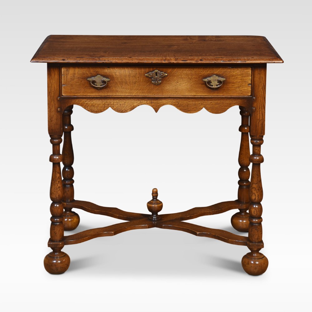 A dark oak side table featuring a single drawer with brass handles, a scalloped apron, turned legs, and an X-shaped cross stretcher. View V