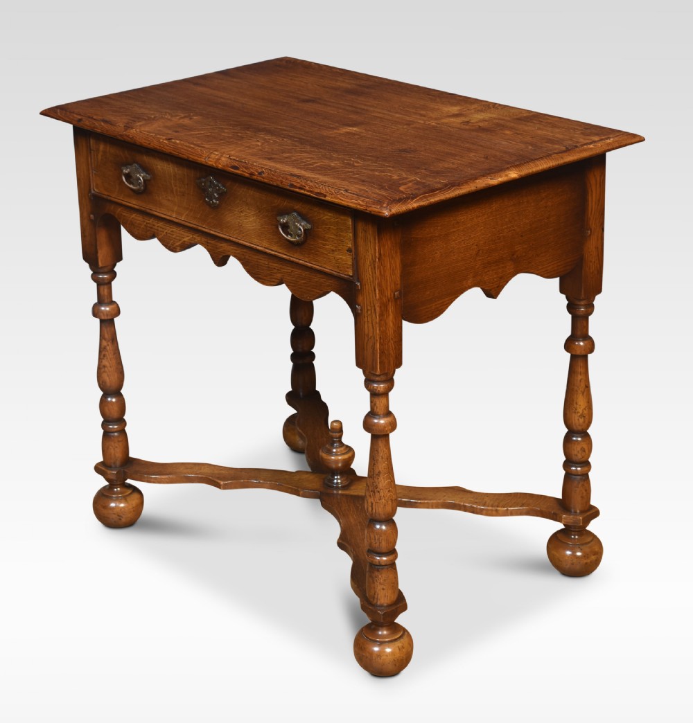 A dark oak side table featuring a single drawer with brass handles, a scalloped apron, turned legs, and an X-shaped cross stretcher. View VI