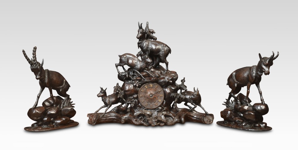 A nineteenth-century Black Forest carved wood mantel clock garniture set featuring sculpted alpine chamois figures atop rocky outcrops.
