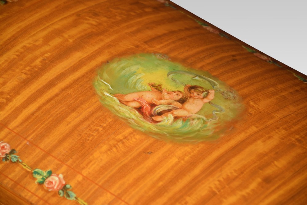 An antique painted satinwood ladies sewing table featuring open lid storage, pleated green silk side panels, and hand-painted floral decorations on tapered legs. View IX