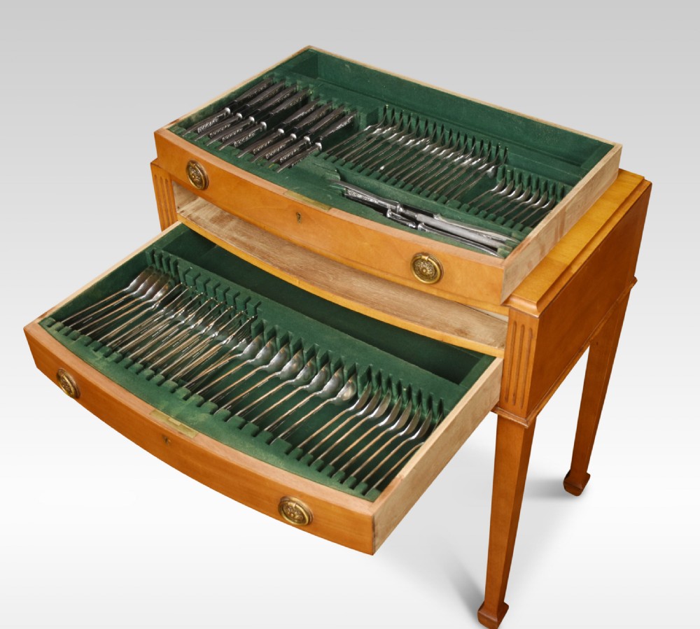 A walnut cutlery canteen table featuring two open drawers lined with green felt filled with silver flatware, resting on tapered legs.