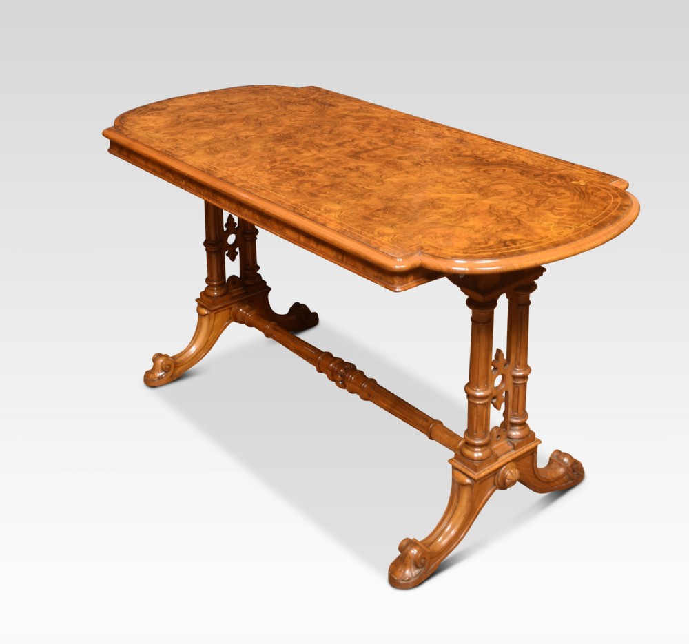 An antique Victorian burr walnut centre table featuring a figured inlaid top, twin turned column supports, a turned stretcher, and carved scrolled feet.