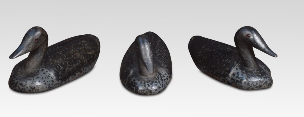 A set of three hand-carved wooden bird decoys painted in dark grey and black with mottled detailing and inset eyes.