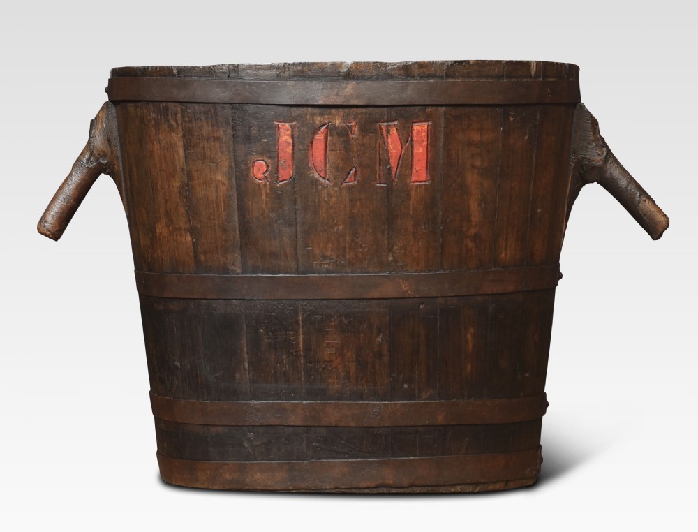 A dark oak coopered log bin featuring angled wooden side handles, hoops, and red carved initials JCM on the front.
