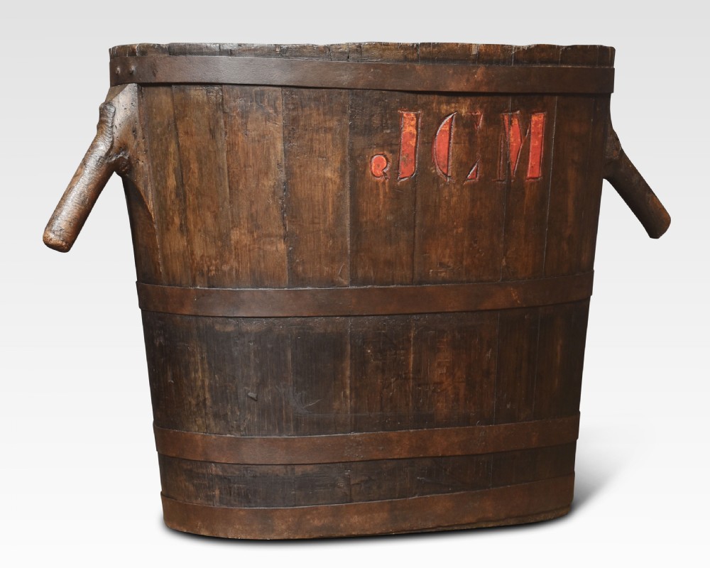 A dark oak coopered log bin featuring angled wooden side handles, hoops, and red carved initials JCM on the front. View II
