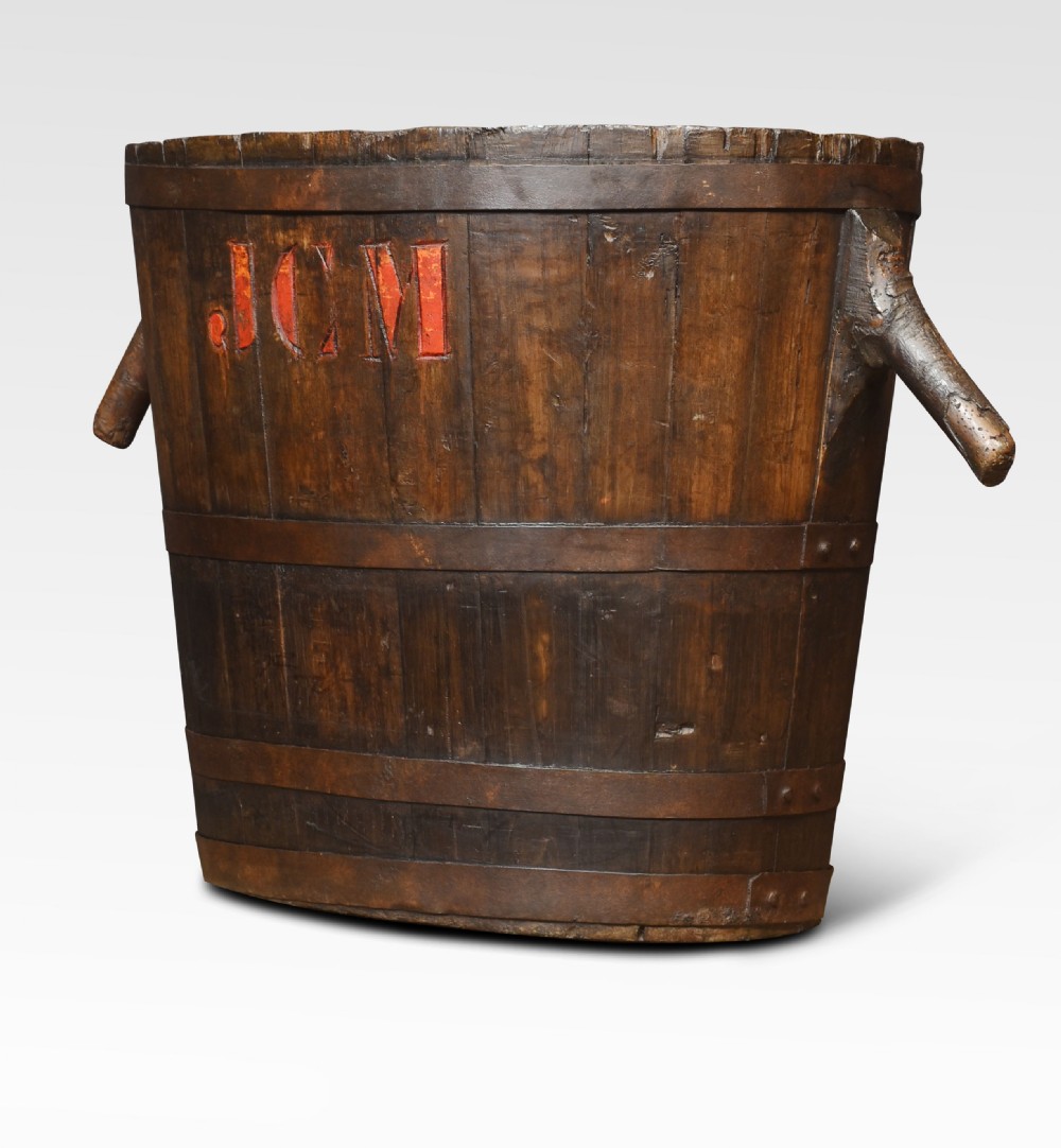 A dark oak coopered log bin featuring angled wooden side handles, hoops, and red carved initials JCM on the front. View III