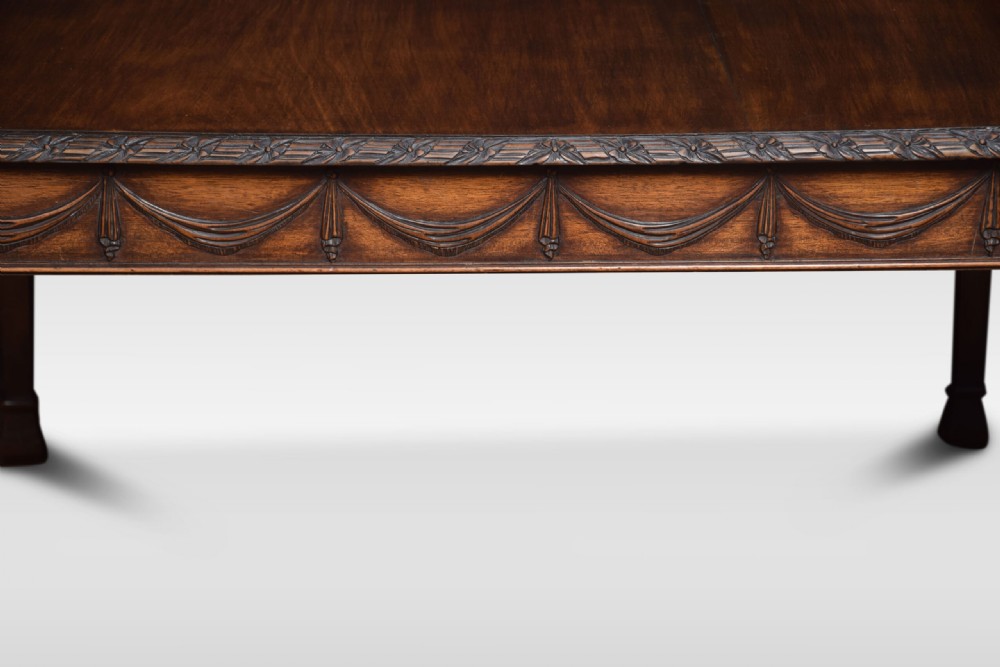 An Adam Revival mahogany centre table featuring a square top with carved edge moulding, a drapery-carved apron, and four tapered square legs. View V