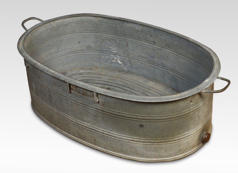 An oval galvanised steel bath tub featuring side carrying handles, ribbed horizontal reinforcement bands, a rolled rim, and a drainage plug near the base. View IV